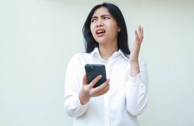 Ne? Asyalı iş kadınının şaşkın bakışları, aklı karışmış akıllı telefonu tutması, kötü haber alması, sosyal medya, beyaz takım elbise giymiş avuç içlerini kaldırması, ayakta durması...