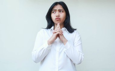 Beyaz takım elbiseli Asyalı genç kadın yöneticinin tasviri. Bir şey düşünüyor. Parmakları çenesinde, endişeli, hayal kuran bir hareket.