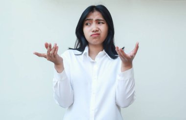 Ne oluyor? Kafası karışmış Asyalı kadın yöneticinin portresi. Problemi omuz silkerek çözmeyi düşünüyor. Avuçlarınızı yana çevirin.