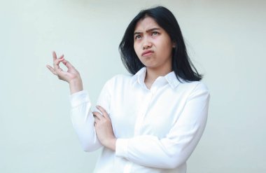 Düşünceli Asyalı genç iş kadını görüntüsü beyaz resmi gömlek giyer kollarını kavuşturup ellerini kaldırarak ve el hareketlerini sergileyerek yukarı bakar.