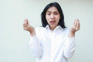 Kafası karışmış Asyalı genç iş kadını yöneticisinin portresi kameraya bakıyor kollarını kaldırıp kıvrılmış parmaklarıyla beyaz resmi tişört giyiyor, sorgulama hareketi yapıyor.