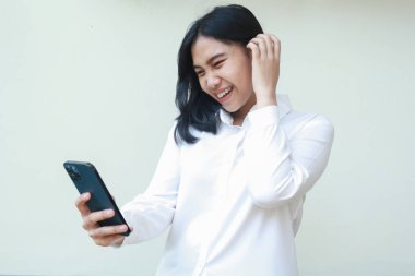 Neşeli, neşeli Asyalı iş kadını gülüyordu. Akıllı telefon uygulamaları kullanıyordu. Koyu renk saçlarının arasından parmağını kaldırıyordu.