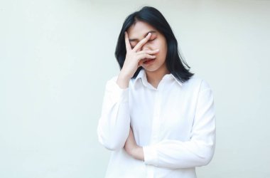 Yorgun Asyalı iş kadınının portresi. Fazla mesai yapmaktan, elleriyle yüzünü kapatmaktan, kollarını kavuşturmaktan, beyaz gömlek giymekten, uykuda poz vermekten, izole edilmiş arka planda durmaktan bıkmış.
