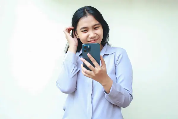 Zarif Asyalı genç iş kadını video araması için akıllı telefon kullanarak kadınlığını gösteriyor, iyi haberler okuyor ve sosyal medya online alışveriş yapıyor, beyaz arka planda duran resmi tişört giyiyor, ekranda