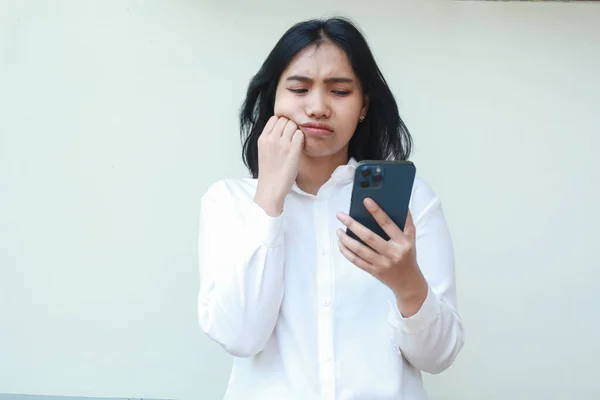 Endişeli Asyalı genç iş kadınlarının çekimleri sorunlu, akıllı telefon teknolojisini kullanarak yanağında yumruk pompası olan, izole edilmiş arka planda duran resmi beyaz takım elbise giyen bir plan.