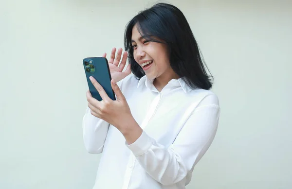 image of success excited young asian saleswoman holding smartphone waving palms say hi welcoming gesture wearing white suit shirt, playful female said hello in social media, video call, standing
