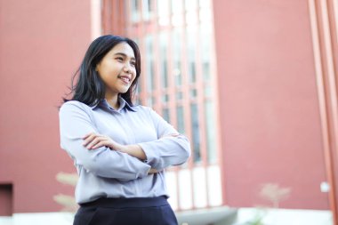 Asyalı başarılı bir iş kadınının resmi tişörtü ile ofis binasının tepesinde dikilmesi, kadın girişimcinin kendinden emin gülümsemesi iyimser bir bakış açısı sergiliyor.