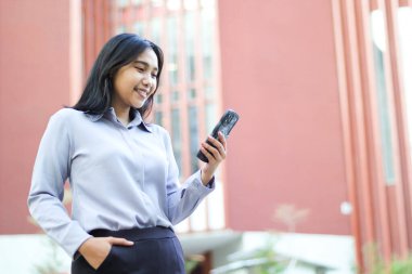 Başarılı iş kadını muhasebeci yönetici ofis binasının üzerinde yürüyor akıllı telefondaki uygulamayı kullanıyor, sosyal medyayı okuyor, resmi takım elbise giyiyor.