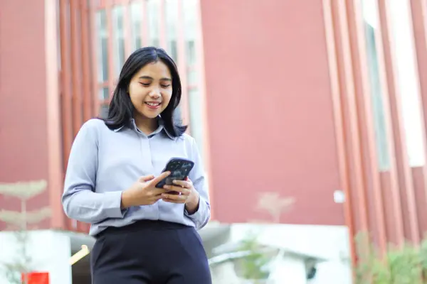 Başarılı iş kadını muhasebeci yönetici ofis binasının üzerinde yürüyor akıllı telefondaki uygulamayı kullanıyor, sosyal medyayı okuyor, resmi takım elbise giyiyor.