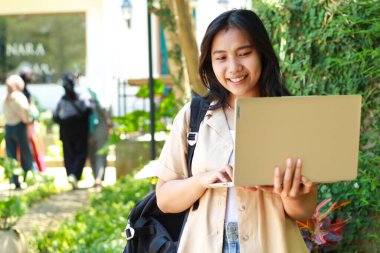 Neşeli Asyalı kadın elinde laptop ve çantasıyla açık kafede dikiliyor günlük şık kıyafetler giyiyor, kadın dijital göçebe, küçük işletme sahibi.