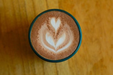 Tahta masada servis edilen yeşil bardakta sıcak latte 'nin üst görüntüsü.