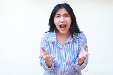 Mavi çizgili tişört giyen kızgın Asyalı kadın çığlık atıyor ve elleri beyaz arka planda tek başına kameraya bakıyor.