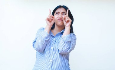 Kafası karışmış Asyalı kadın, sıradan çizgili tişört giyip boş bir yeri işaret ederek izole edilmiş beyaz arka planda duran seçenekleri düşünüyor.