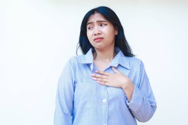 Kafası karışmış Asyalı kadın göğsüne dokunarak şok oldu. Mavi çizgili gömlek giyiyordu. İzole edilmiş beyaz arka planda duruyordu.