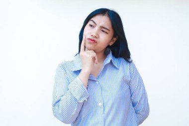 Kafası karışmış Asyalı kadın beyaz arka planda izole edilmiş çizgili gömlek giyerek düşünceli görünüyor.
