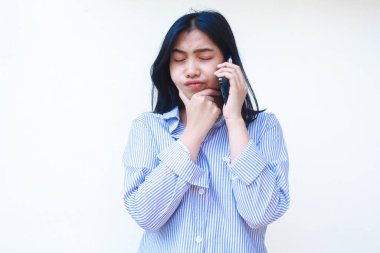 Akıllı telefon kullanan düşünceli Asyalı kadın çene düşünme problemi yaşıyor mavi çizgili günlük gömlek giyiyor izole beyaz arka planda dikiliyor, başka tarafa bak.