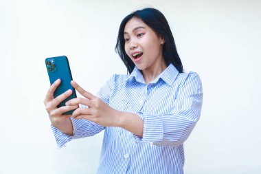 Mutlu Asyalı kadın beyaz arka planda izole edilmiş çizgili gömlek giyerek akıllı telefon kullanarak şok oldu.