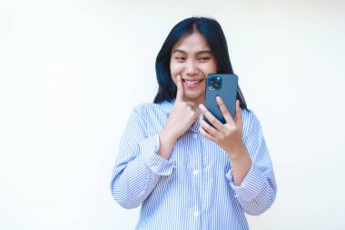 Sosyal medyada akıllı telefon sörfü yapan mutlu Asyalı kadın beyaz arka planda izole edilmiş çizgili gömlek giyiyor.