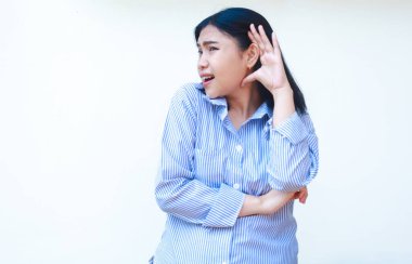 Şok olmuş Asyalı kadın, beyaz arka planda izole edilmiş çizgili gömlek giymiş, kulaklarının yanında avuç içi kaldırarak gizlice dinliyor.