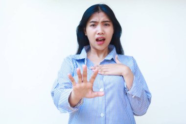 Şok olmuş Asyalı kadın göğsüne dokunuyor ve ellerini öne uzatıyor. Beyaz arka planda izole edilmiş çizgili gömlek giyiyor.