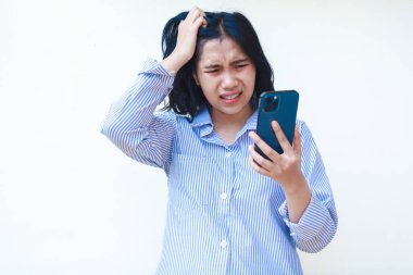 Şok olmuş Asyalı kadın beyaz arka planda izole edilmiş çizgili gömlek giymiş ağzı açık bir şekilde akıllı telefon kullanıyor.