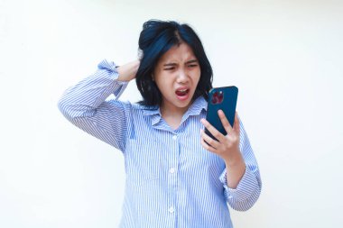 Şok olmuş Asyalı kadın beyaz arka planda izole edilmiş çizgili gömlek giymiş ağzı açık bir şekilde akıllı telefon kullanıyor.