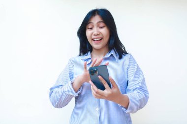 Mutlu Asyalı kadın cep telefonuyla konuşurken şaşırdı. Beyaz arka planda izole edilmiş çizgili gömlek giyiyordu.