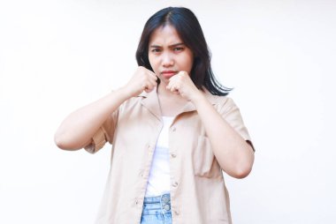 Kızgın Asyalı kadın yumruğunu kaldırdı ve jest yapmaya hazır beyaz arka planda izole edilmiş günlük kıyafetler giyiyor.