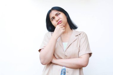 Düşünceli Asyalı kadın gündelik kıyafetler giyiyor. Düşüncelerini düşünüyor ve elleri çenesinde ve kolları beyaz arka planda soyutlanmış bir şekilde merak ediyor.