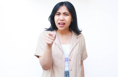 Düşünceli Asyalı kadın, beyaz arka planda izole edilmiş günlük kıyafetler giyen kafası karışık bir yüz ifadesini işaret ediyor.