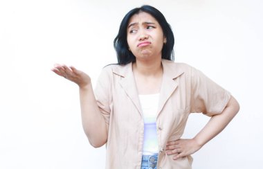 Asyalı düşünceli bir kadın, beyaz arka planda izole edilmiş günlük kıyafetler giyerek el hareketlerini açık ve kafası karışmış bir şekilde sunuyor.