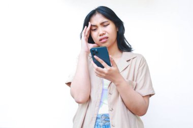 Düşünceli Asyalı kadın, beyaz arka planda izole edilmiş günlük kıyafetler giyen akıllı telefon kullanarak kafası karışmış görünüyor.
