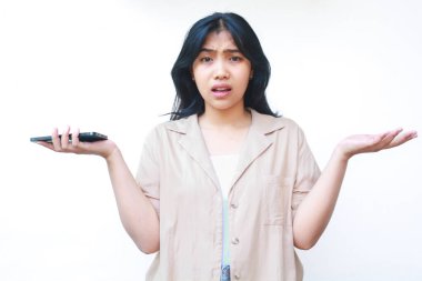 Kafası karışmış Asyalı kadın, avuçlarını kaldırmış akıllı telefon kullanıyor. Belirsizlik işareti, beyaz arka planda izole edilmiş günlük kıyafetler giyiyor.