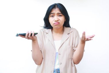 Kafası karışmış Asyalı kadın, avuçlarını kaldırmış akıllı telefon kullanıyor. Belirsizlik işareti, beyaz arka planda izole edilmiş günlük kıyafetler giyiyor.