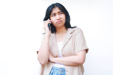 Kafası karışık Asyalı kadınlar, beyaz arka planda izole edilmiş günlük kıyafetler giyen akıllı telefonlardan aranıyorlar.