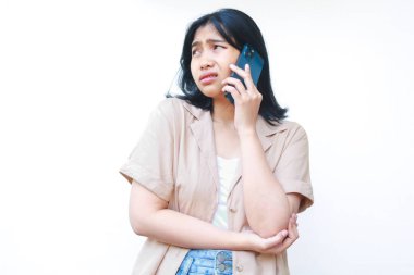 Kafası karışık Asyalı kadınlar, beyaz arka planda izole edilmiş günlük kıyafetler giyen akıllı telefonlardan aranıyorlar.