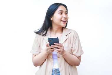 Heyecanlı Asyalı kadın akıllı telefon kullanıyor ve beyaz tenli, günlük kahverengi elbiseler giyiyor.