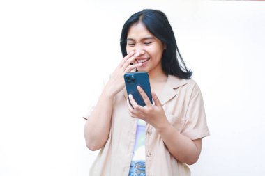 Akıllı telefon kullanırken gülümseyen heyecanlı Asyalı kadın beyaz arka planda günlük kahverengi giyiyordu.