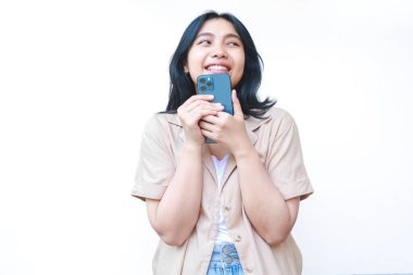 Heyecanlı Asyalı kadın akıllı telefon kullanıyor ve beyaz tenli, günlük kahverengi elbiseler giyiyor.