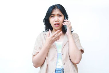 Akıllı telefon tutan Asyalı kadın beyaz arka planda izole edilmiş günlük kıyafetler giyerken çok şaşırmış görünüyor.