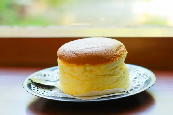 Japon cheesecake 'i yeşil vintage tabakta, pencere kenarında ahşap masada servis ediliyor.