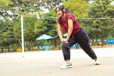 Asyalı kadın voleybol sahasında gün ortasında bacağını esnetiyor, kadın egzersizden önce ısınıyor.