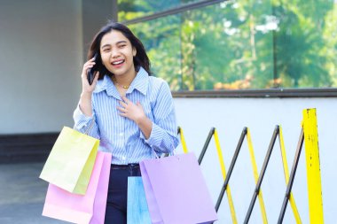 Alış veriş torbası tutan Asyalı kadın şaşırdı ve cep telefonuyla konuşuyor. Şehir merkezinin etrafında yürürken göğsüne dokunuyor.
