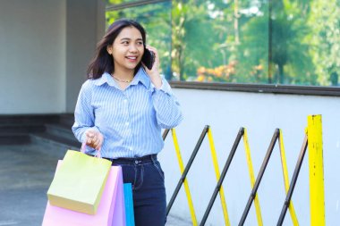 Elinde alışveriş çantası olan gülümseyen Asyalı kadın şehir merkezinde dolaşırken cep telefonundan aranmış.