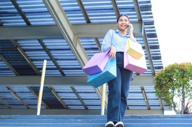 Gülümseyen Asyalı kadının açık havada şehir merdivenlerinde yürürken cep telefonuyla konuşmasının düşük açılı görüntüsü