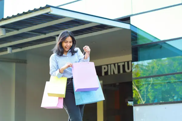 laughing asian woman holding shopping bag walking in outdoors