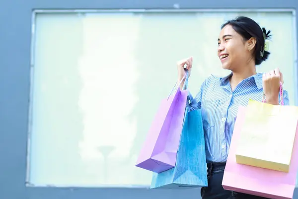 laughing asian woman holding shopping bag walking in outdoors with empty billboard background