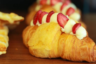 Kahverengi kruvasan, çilekli ve dondurmalı, ahşap kahve dükkanı rafında, seçici odaklı.