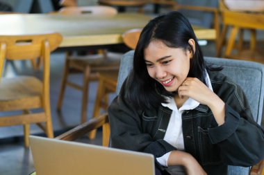 Neşeli Asyalı kadın kapalı kafede online toplantı videosu yapmak için laptop kullanıyor.