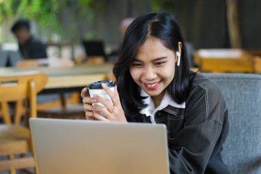 heyecanlı Asyalı kadın kahve içiyor ve bilgisayarı kullanarak kafede dijital göçebe toplantı yapıyor.